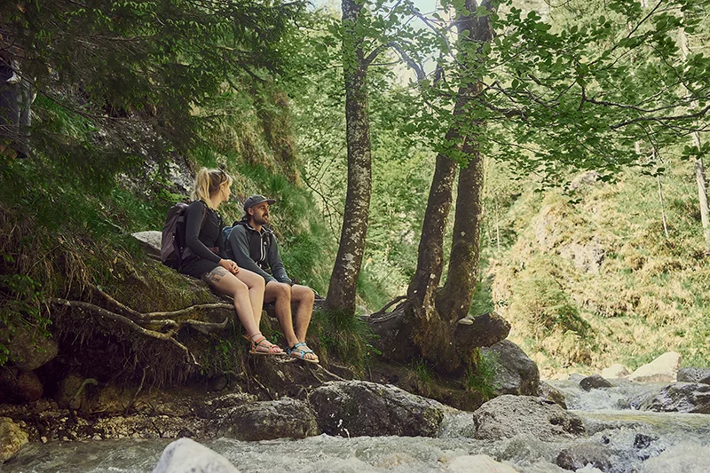 pärchen sitzt mit trekkingsandalen am bergbach