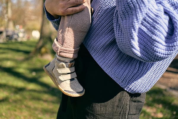 kleinkind mit lauflernschuhen wird von der mama getragen