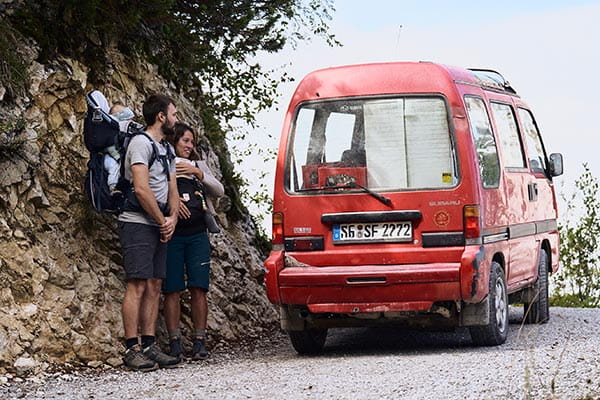 auto fährt auf enger bergstraße an zwei wanderern mit trekking barfußschuhen vorbei